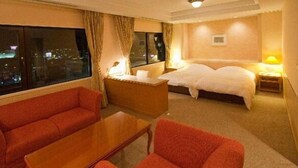 A hotel room with a large window, a sofa, a bed, and a nightstand with a lamp. - Grand Plaza Nakatsu Hotel (Nakatsu)