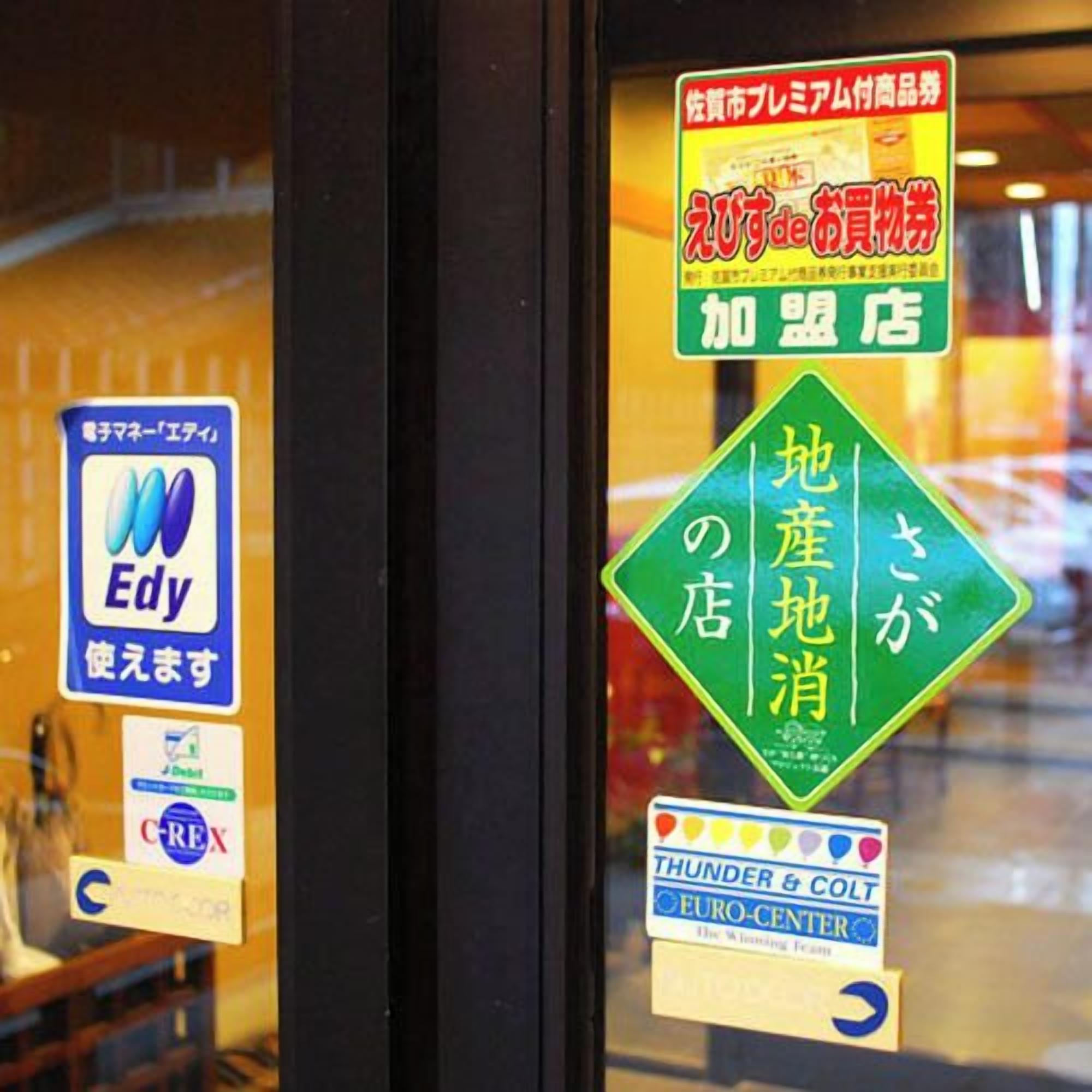 A hotel window with various stickers, including one for Edy, a sign for Thunder & Colt Euro-Center, and a green sign with Japanese text.
