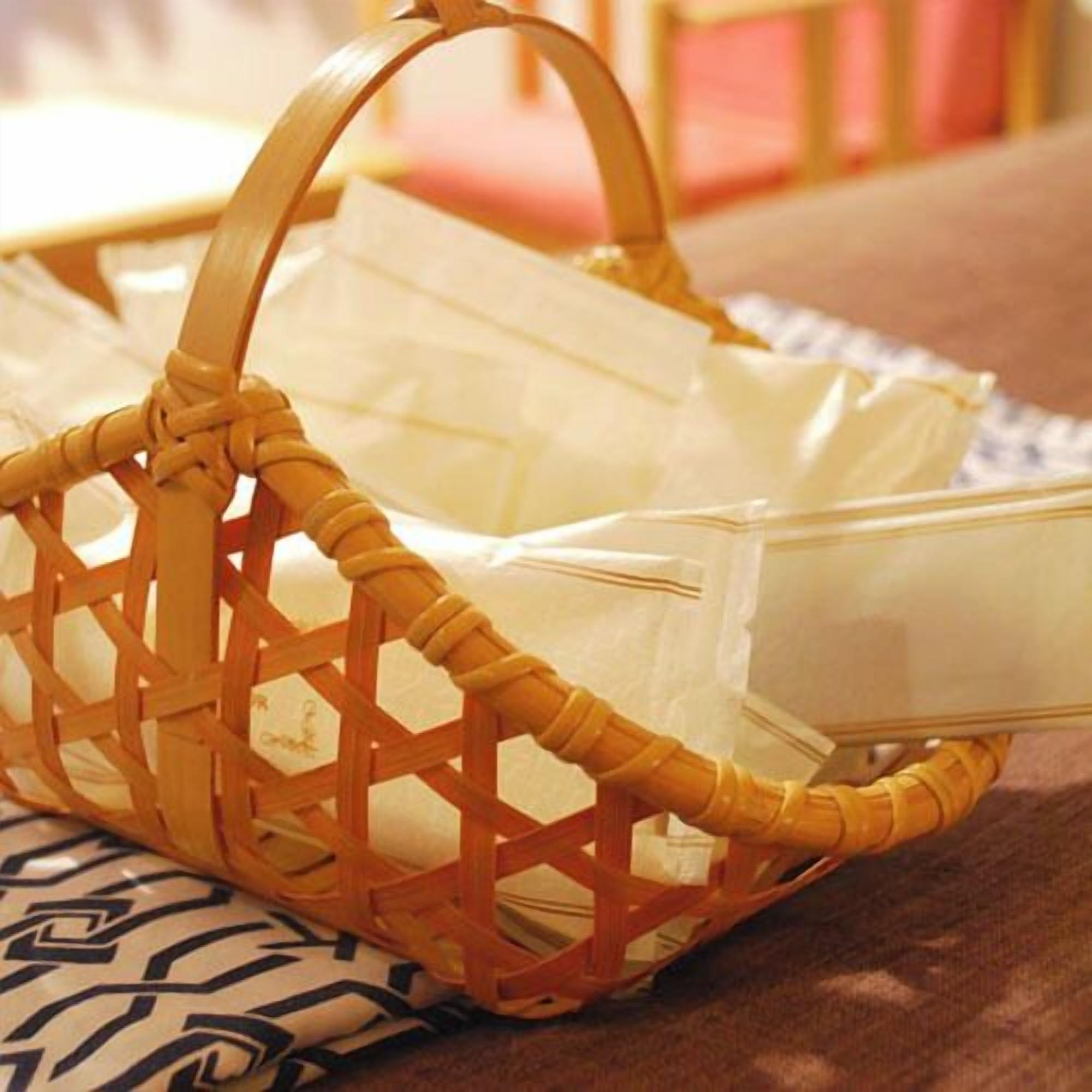 A wicker basket with handles containing a white plastic bag and a clear plastic container.