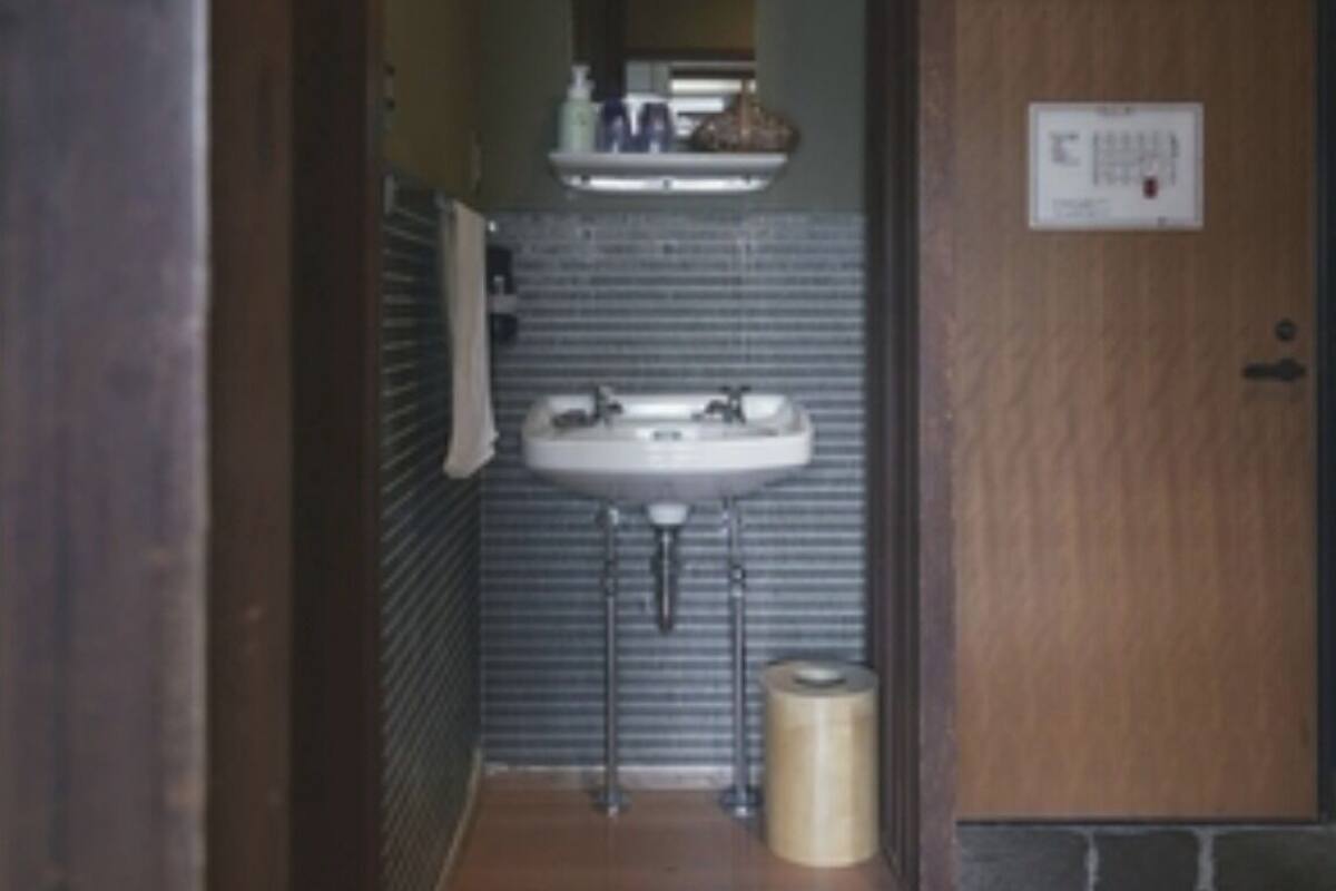 Un couloir étroit mène à une salle de bain équipée d’un lavabo, d’un porte-serviettes et d’une poubelle.