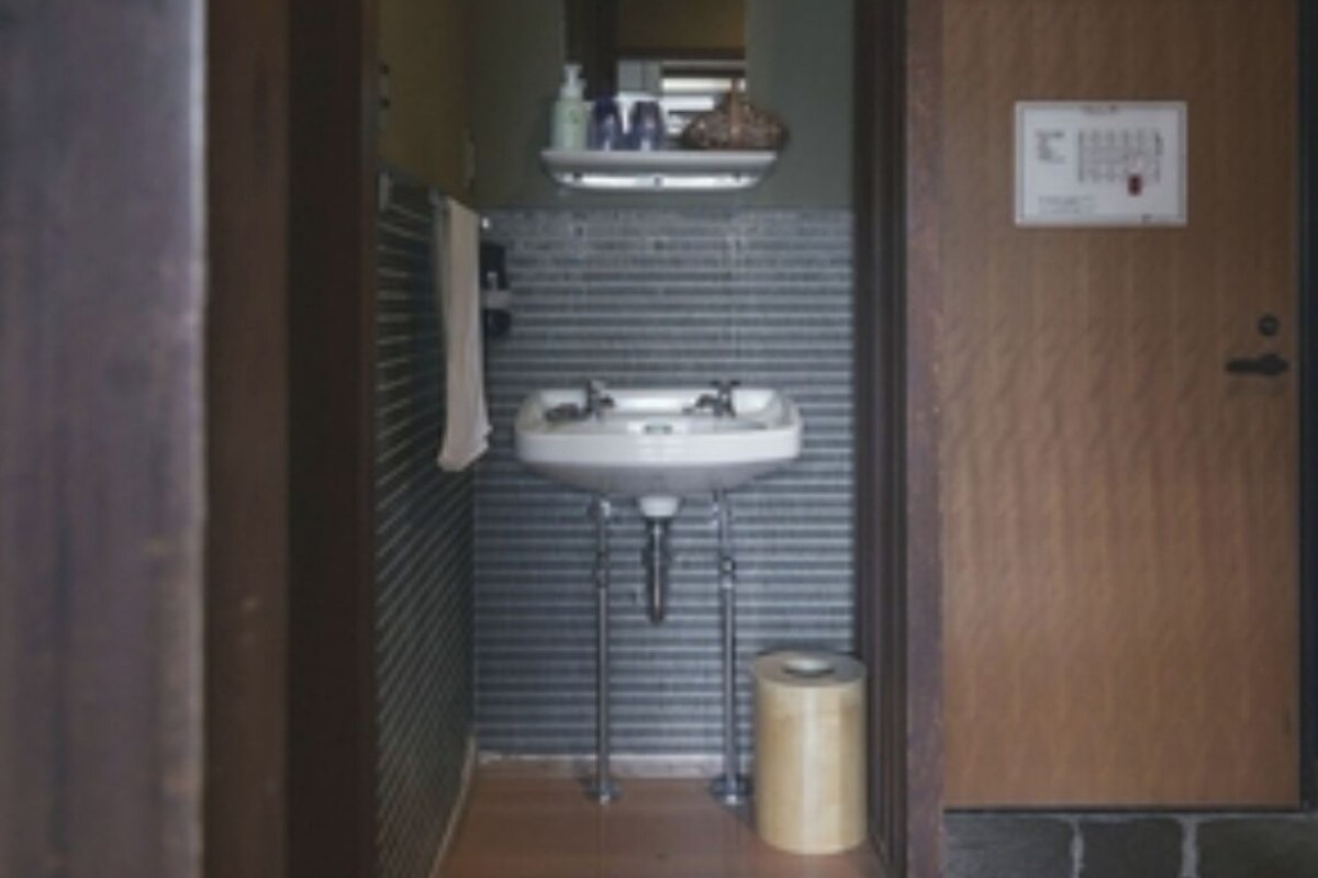 Un pasillo estrecho que conduce a un baño con un lavabo, un perchero para toallas y un cubo de basura.