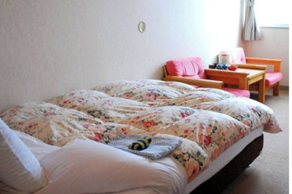 Une chambre à coucher avec un lit, une chaise, une table et une fenêtre.