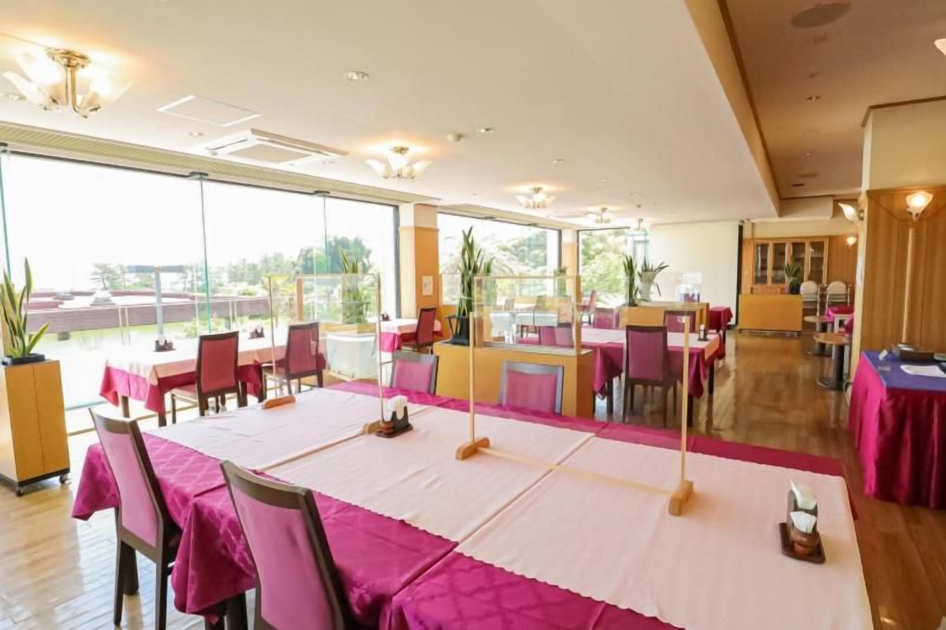 A dining area with tables set for service, large windows, and a view of the outdoors.