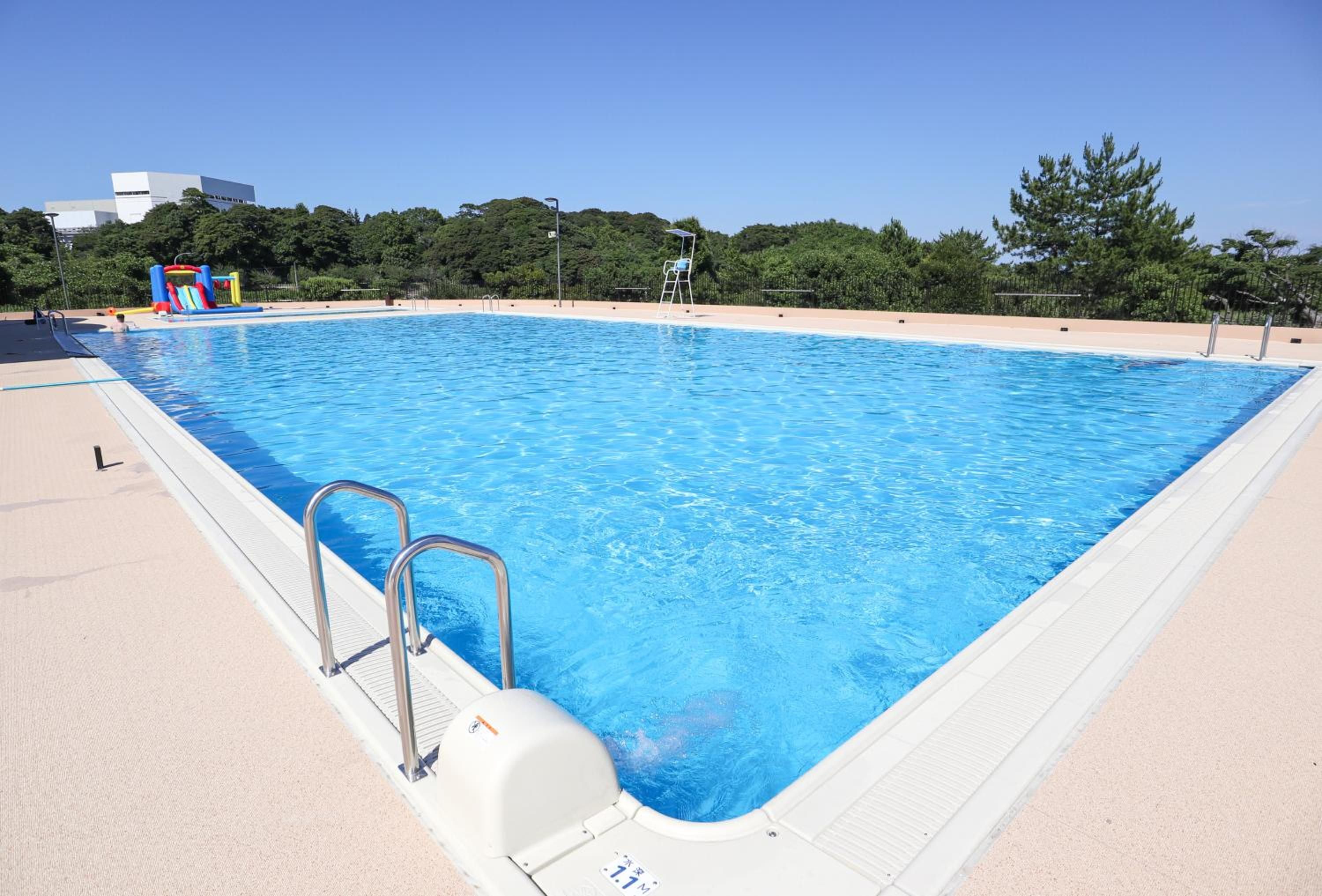 A rectangular swimming pool with a clear blue water surface, surrounded by a sandy deck.