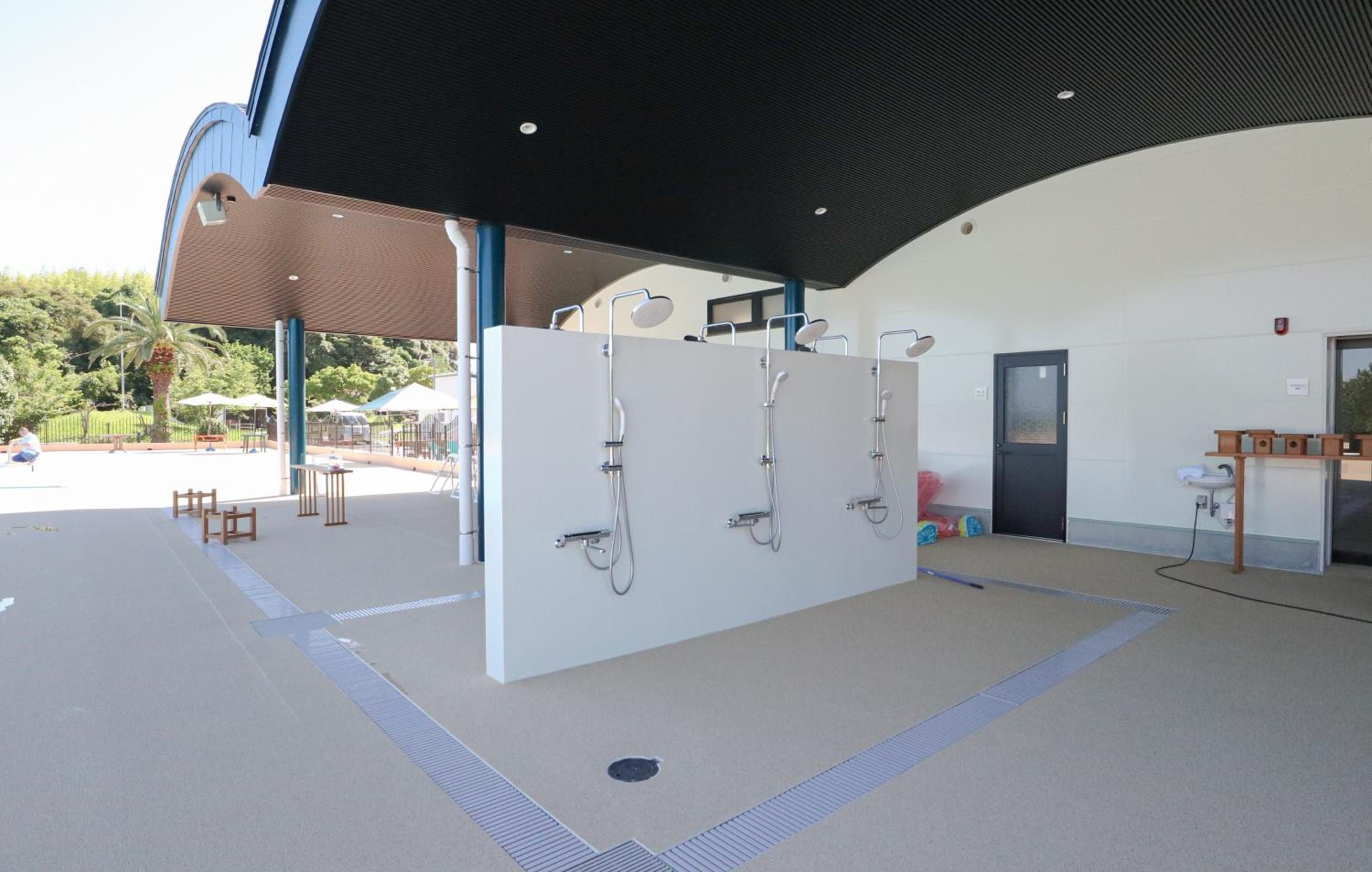 A covered outdoor area with a modern shower station, seating, and a view of the surrounding park.