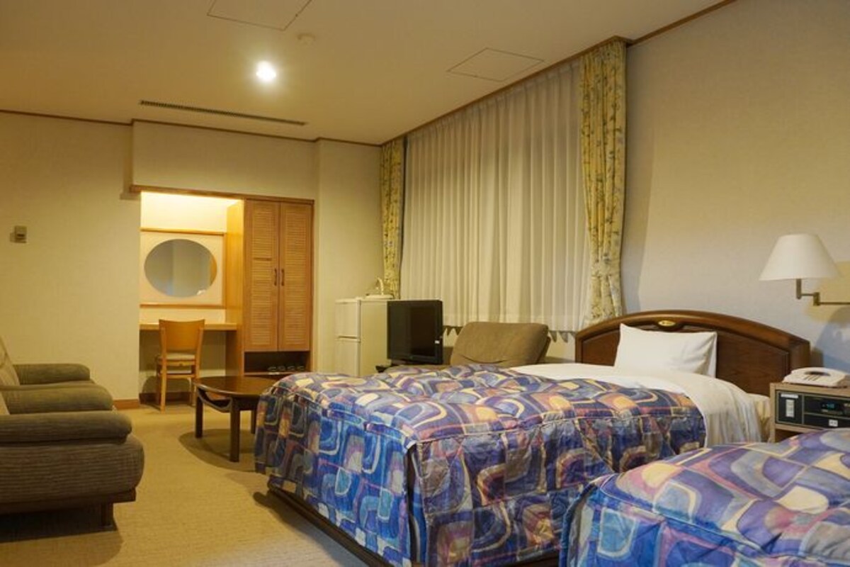 Habitación de hotel con dos camas, un escritorio, una silla, un televisor y un armario.