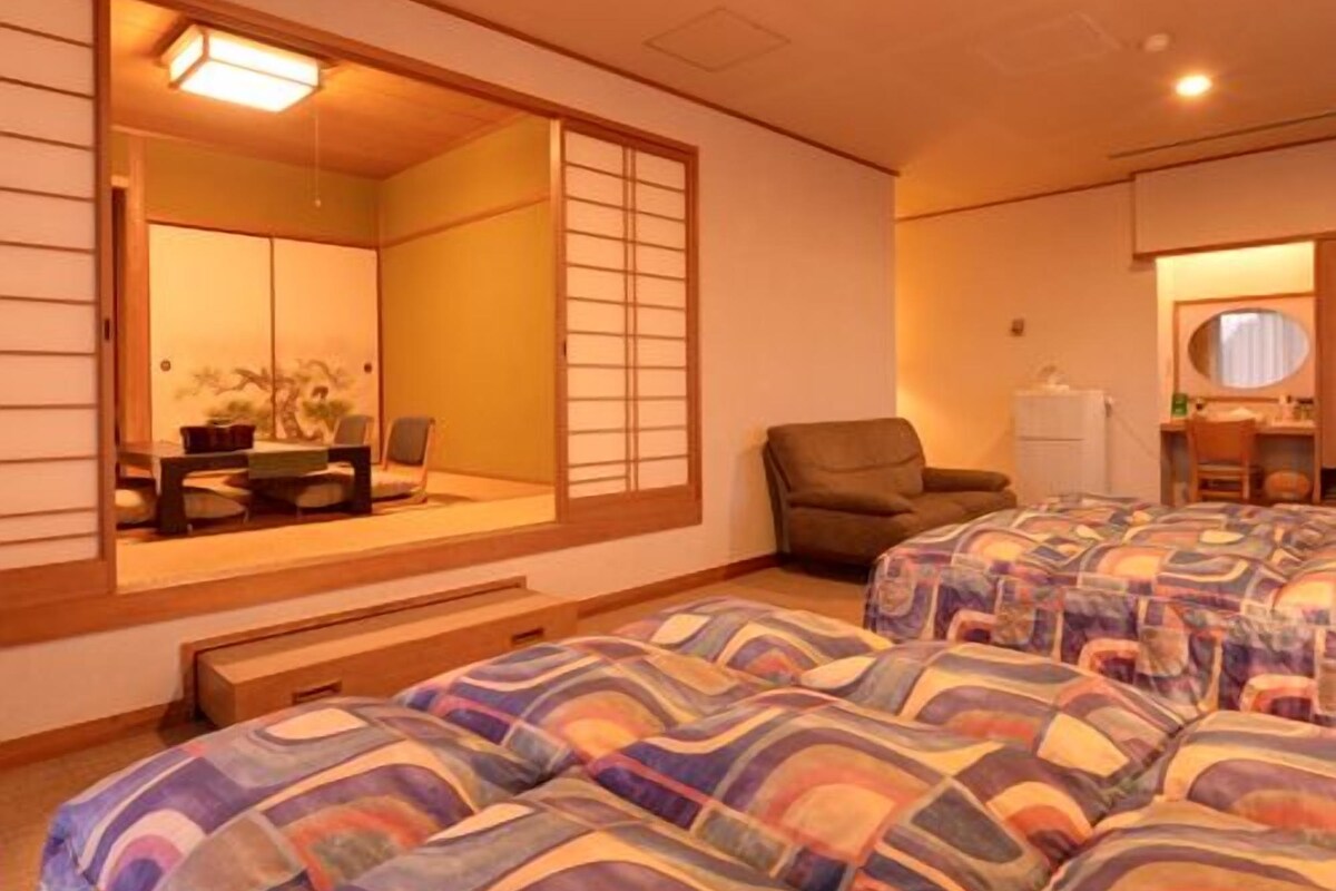 A hotel room with a traditional Japanese sliding door, a sofa, a chair, and a bed with patterned bedding.