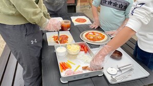 Een groep mensen maakt pizza’s met verschillende ingrediënten op een tafel.