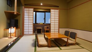 Een traditionele Japanse kamer met tatami vloerbedekking, een lage tafel met kussens, een televisie en verschuifbare shoji schermen.