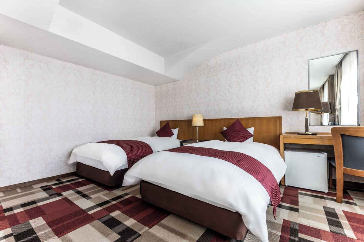 Une chambre d’hôtel avec deux lits, un bureau, une chaise et un petit réfrigérateur.