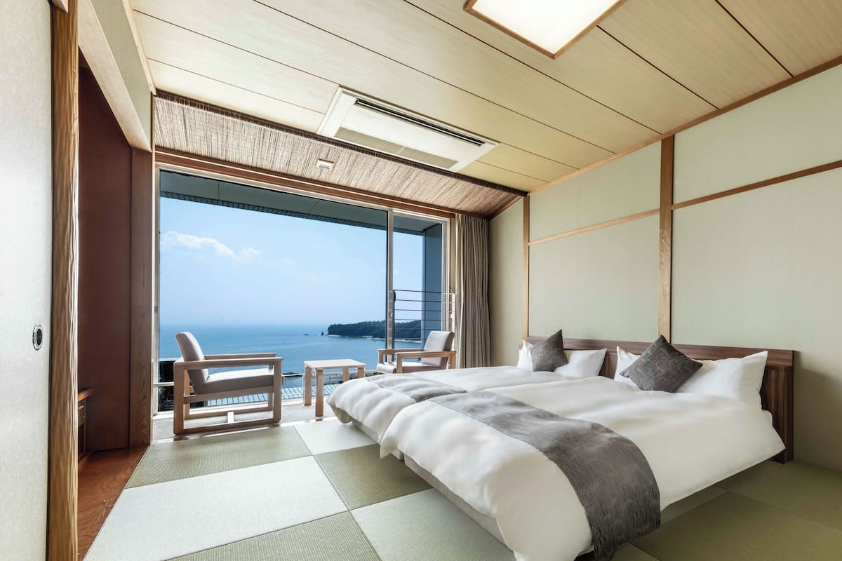Une chambre d’hôtel avec un grand lit, une vue sur la mer et un balcon équipé de chaises.