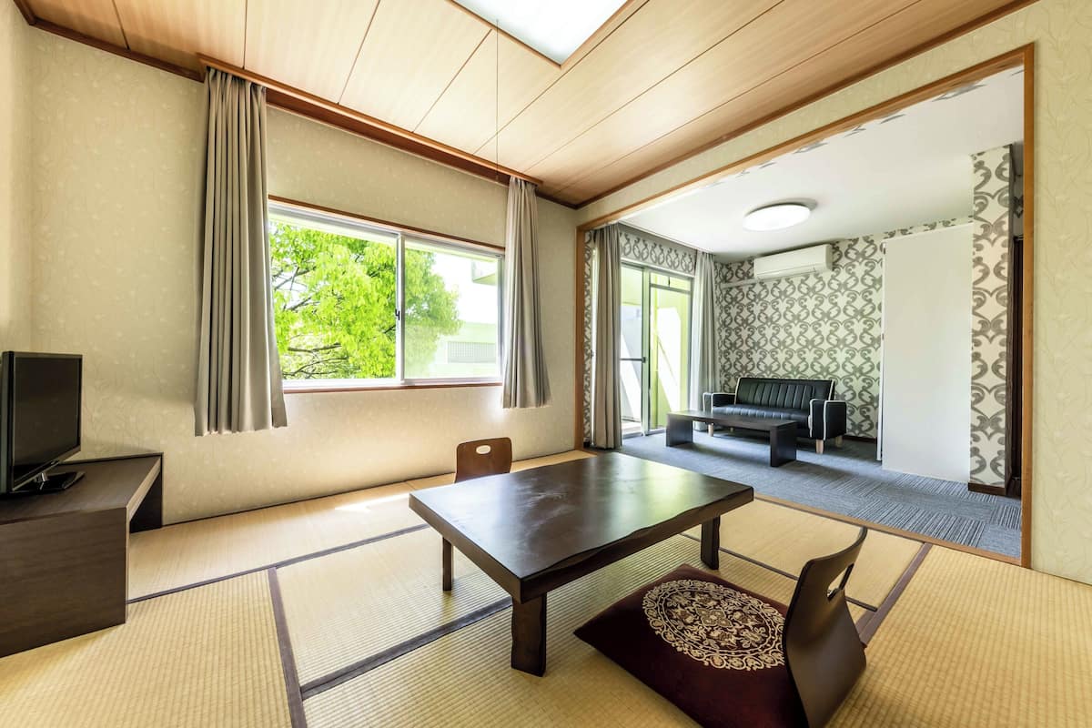 Une pièce de style japonais traditionnel, avec un sol recouvert de tatamis, une table basse, un canapé et un téléviseur.