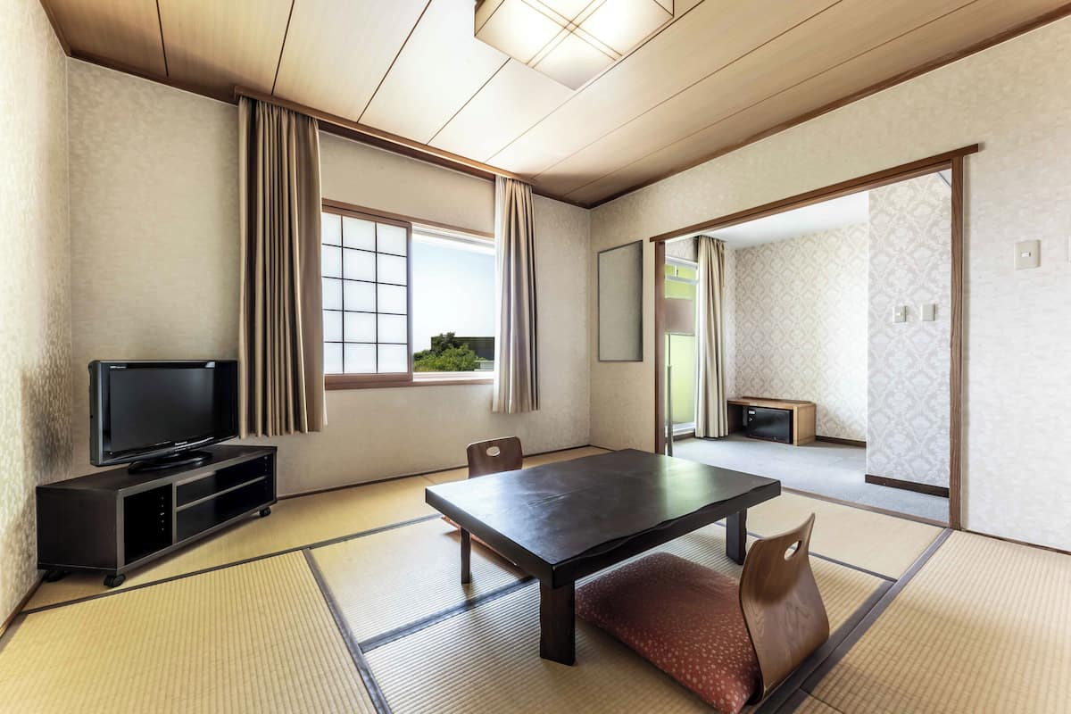 Une pièce de style japonais traditionnel, avec un sol recouvert de tatamis, une table basse, un téléviseur posé sur un meuble et des portes coulissantes donnant sur une autre pièce.