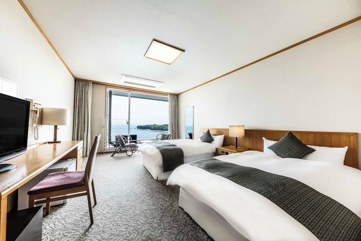 Une chambre d’hôtel avec deux lits, un bureau avec une chaise, une télévision et une vue sur la mer.