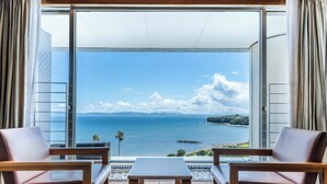 Un balcon avec deux fauteuils en cuir et une petite table, offrant une vue sur la côte, avec un ciel dégagé et une terre lointaine à l’horizon.