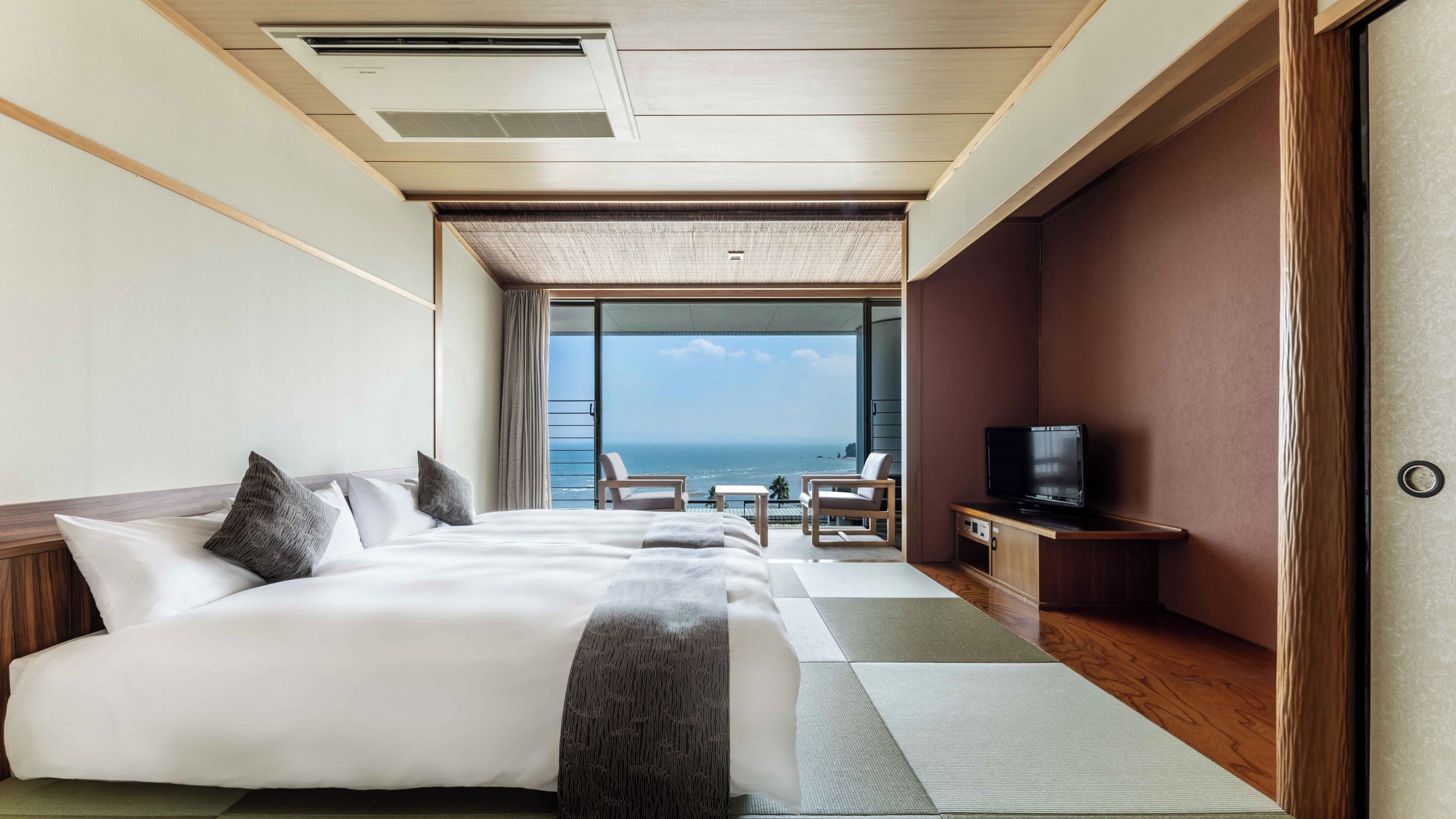 A hotel room with a large bed, a TV, a seating area with a view of the sea, and a balcony.
