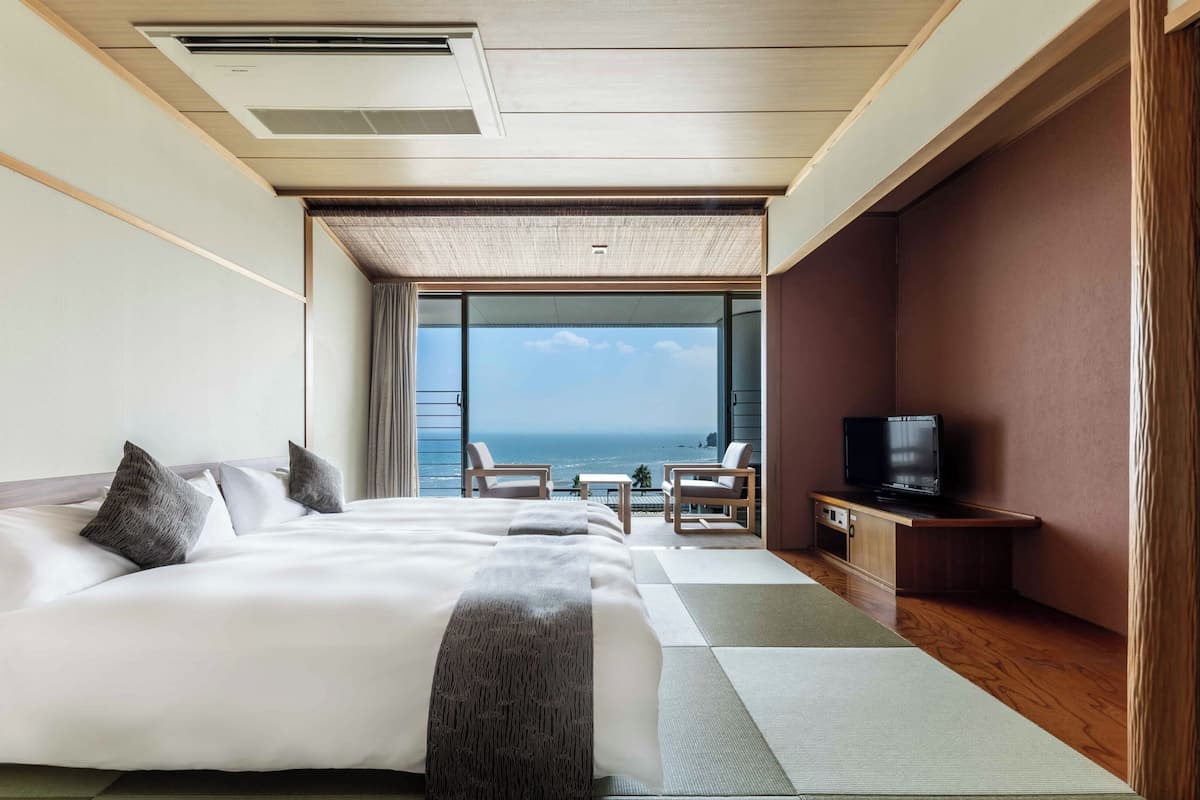 Une chambre d’hôtel dotée d’un grand lit, d’une télévision, d’un coin salon avec vue sur la mer et d’un balcon.