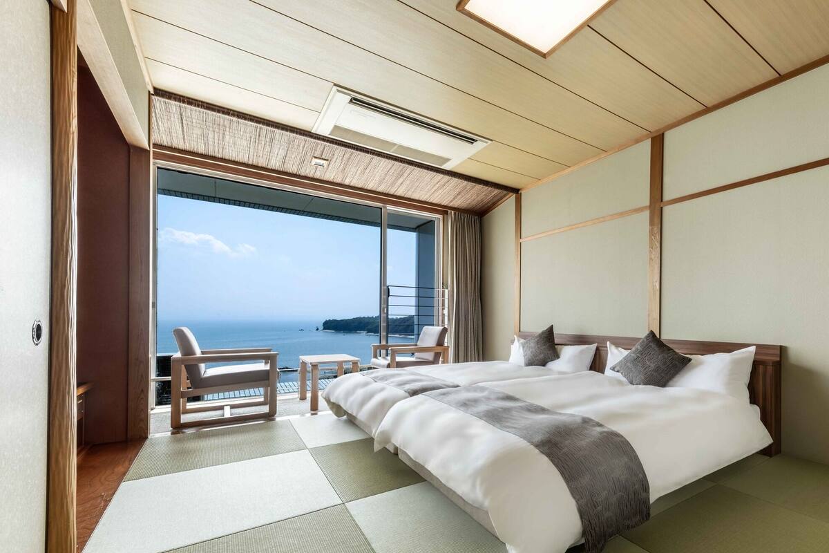 Une chambre d’hôtel avec un grand lit, une vue sur la mer et un balcon équipé de chaises.