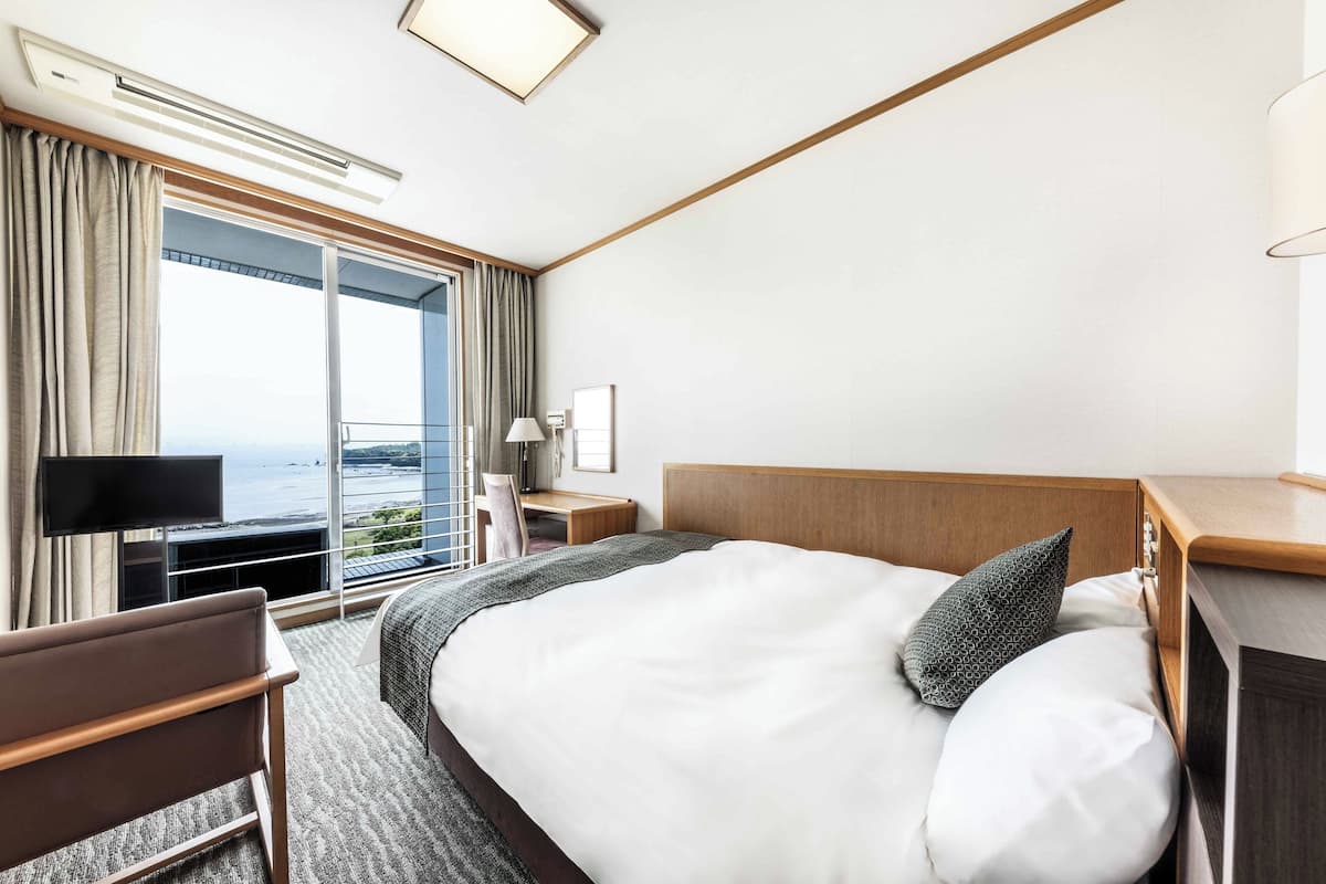 Une chambre d’hôtel avec un grand lit, un bureau, une chaise, une télévision et une vue sur l’océan.