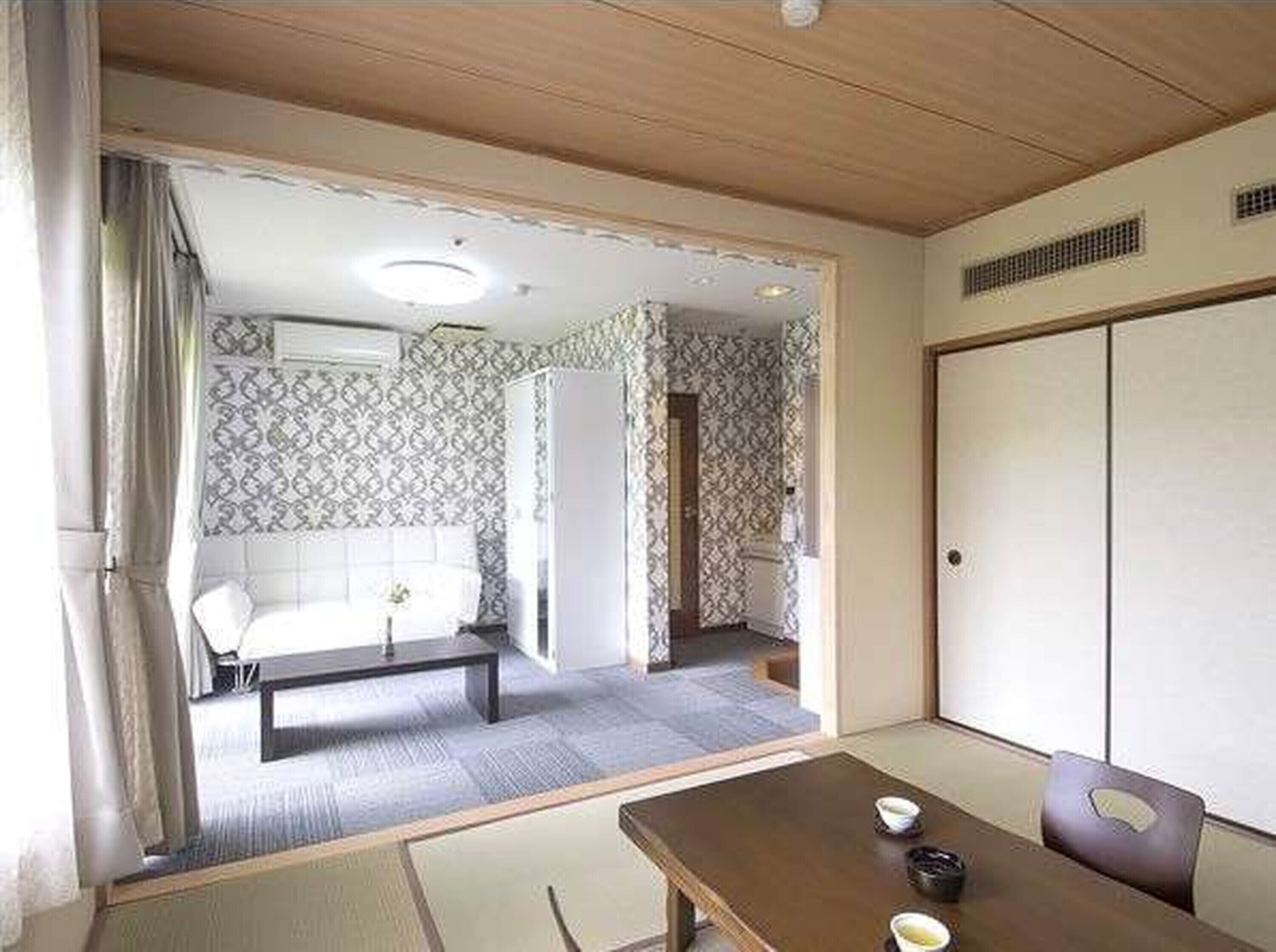 A traditional Japanese-style room with tatami flooring, a low table with a cushion, and a sliding door leading to another room.