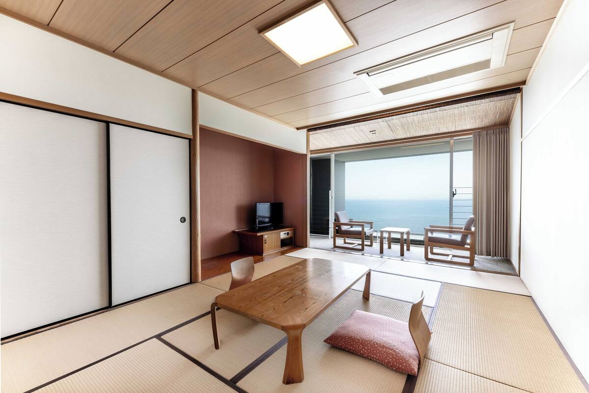 Une pièce avec un sol recouvert de tatamis, une table en bois, un téléviseur et une vue sur la mer.