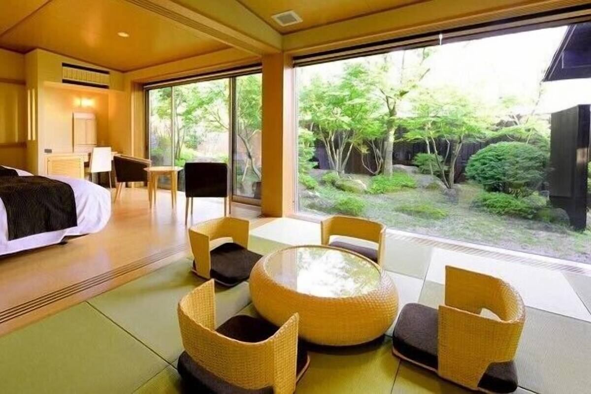 Une chambre d’hôtel avec un lit, une table à manger et des chaises, et une vue sur la verdure.