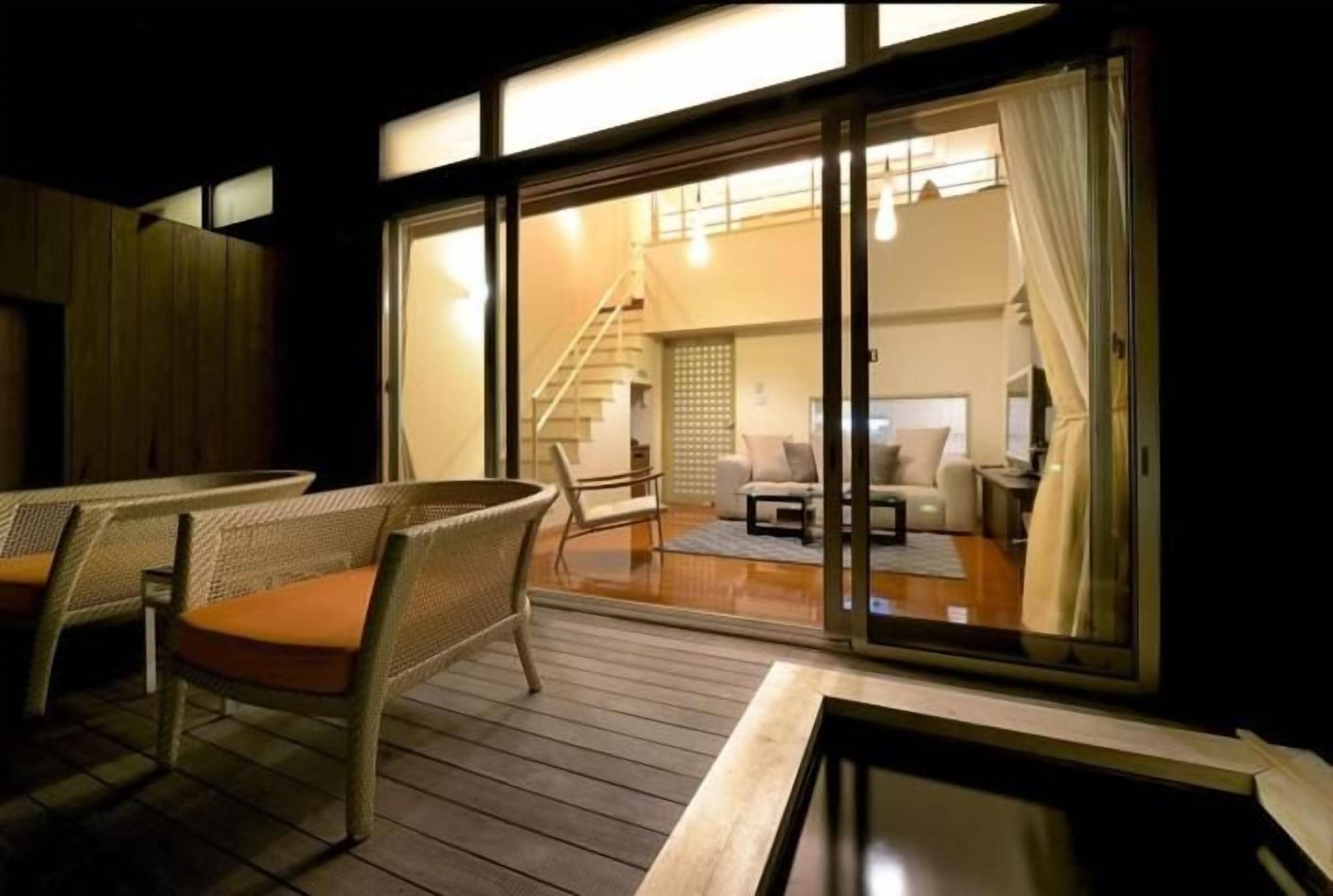 Una habitación con puerta de vidrio corrediza que da a un balcón con mobiliario de mimbre y vista al interior.