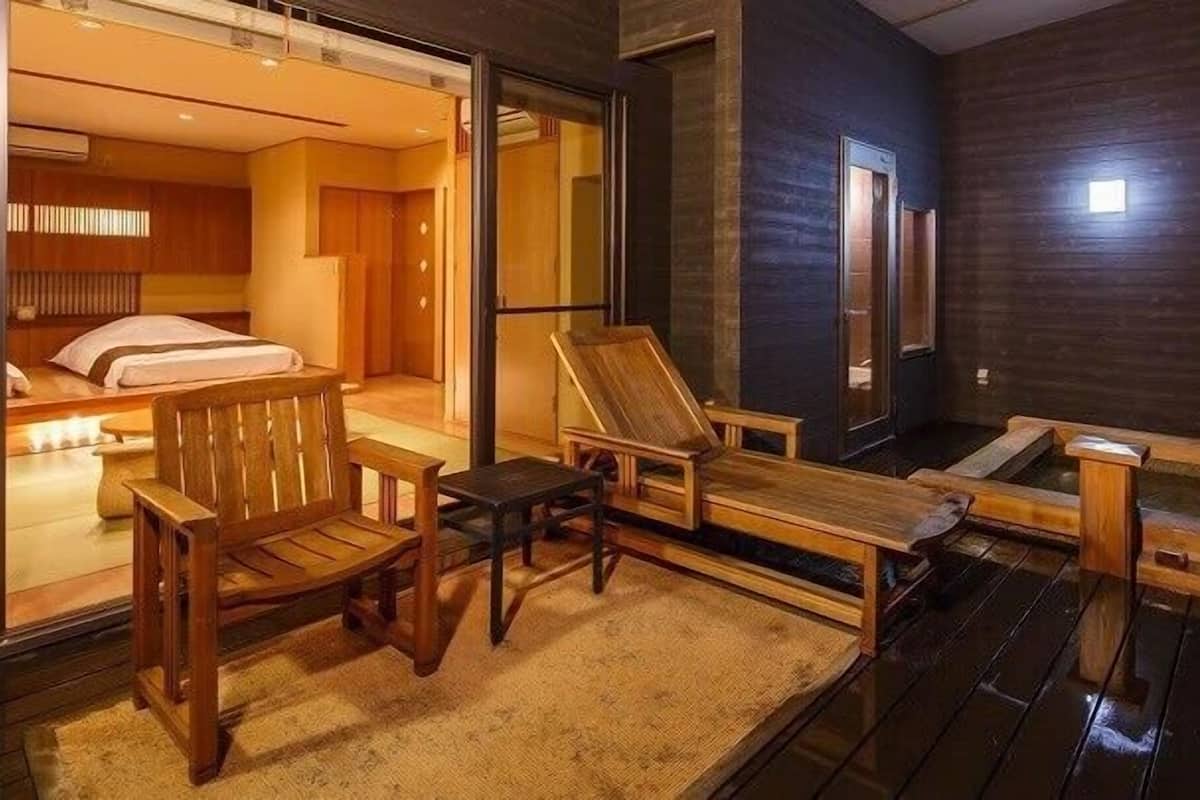 Une terrasse en bois avec un jacuzzi, des chaises longues et une pièce comprenant un lit et une porte coulissante.