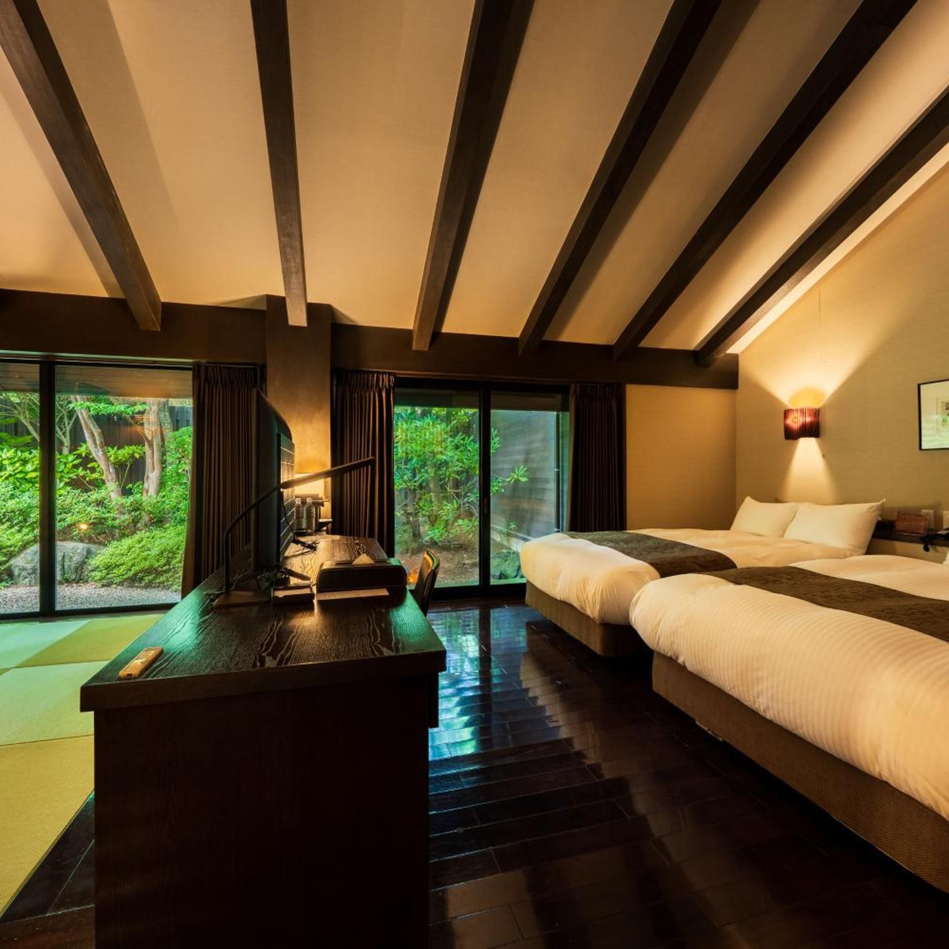 A hotel room with a large bed, a desk, and a view of greenery through the windows.