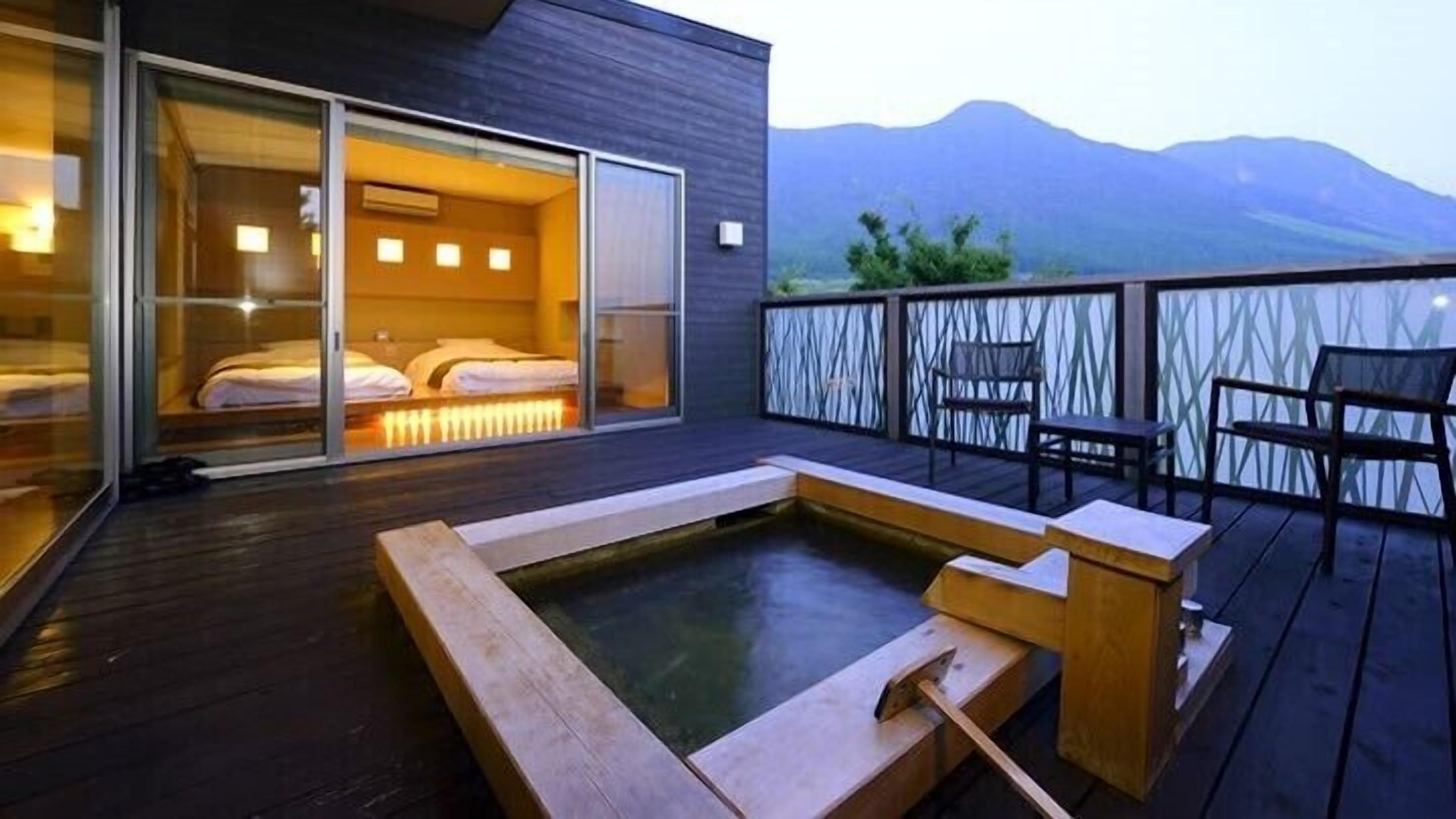 A modern hotel room with a large sliding glass door, a hot tub, and a view of mountains.