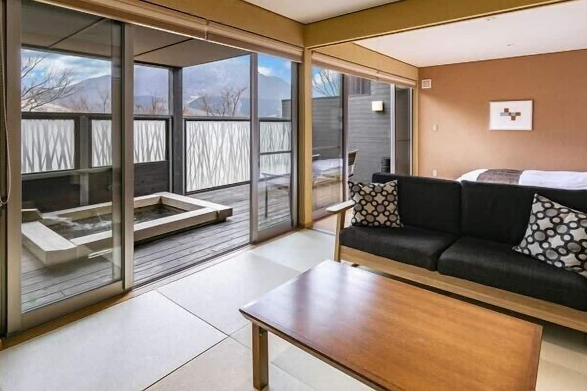 Un intérieur moderne avec une porte-fenêtre coulissante donnant sur une terrasse, un canapé noir agrémenté de coussins à motifs et une table basse en bois.