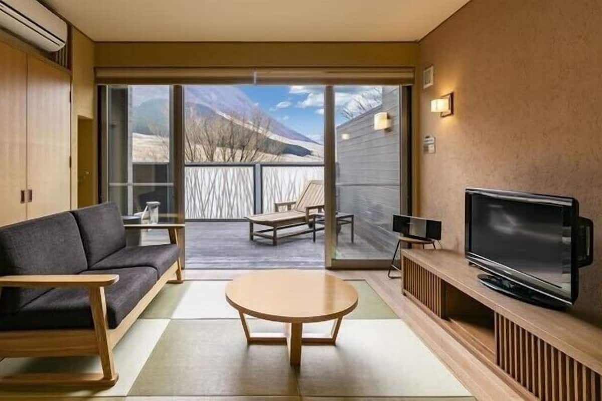 Une pièce comprenant un canapé, une petite table, un téléviseur et une porte-fenêtre coulissante donnant sur un balcon avec vue sur les montagnes.