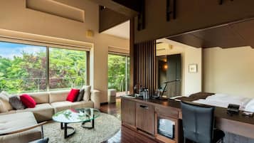 A modern hotel room with a large window, a sofa, a dining area, and a kitchen counter.
