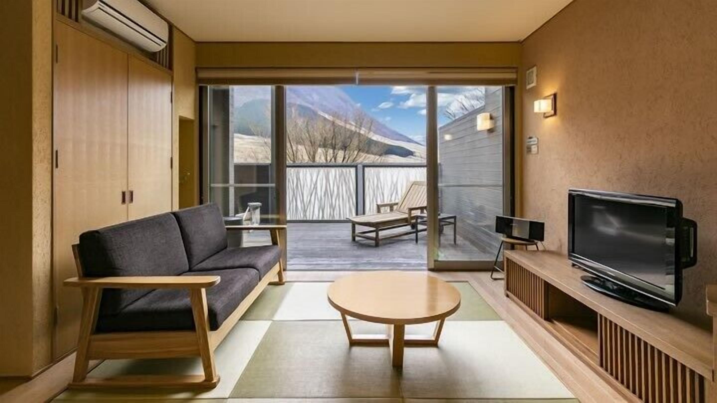 A modern living room with a sofa, coffee table, TV, and a view of mountains through the sliding glass door.
