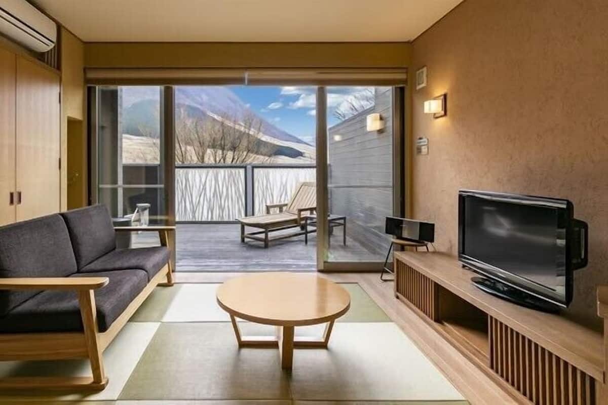 Un salon moderne avec un canapé, une table basse, un téléviseur et une vue sur les montagnes, visible à travers la porte-fenêtre coulissante.