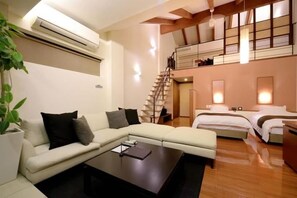 A modern living room with a sofa, a coffee table, and a staircase leading to a loft bedroom. - Okuyado Buaisou (Yufu)