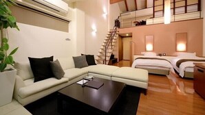 Quarto de hotel moderno com sofá, mesa pequena, cama, escada e planta.