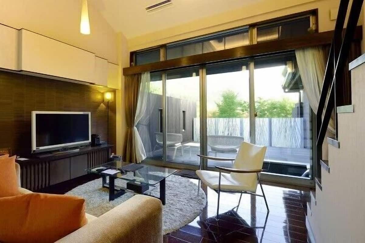 Un salon moderne doté d’un téléviseur à écran plat, d’un canapé et de fauteuils, ainsi que d’une porte vitrée donnant sur un espace extérieur avec vue.