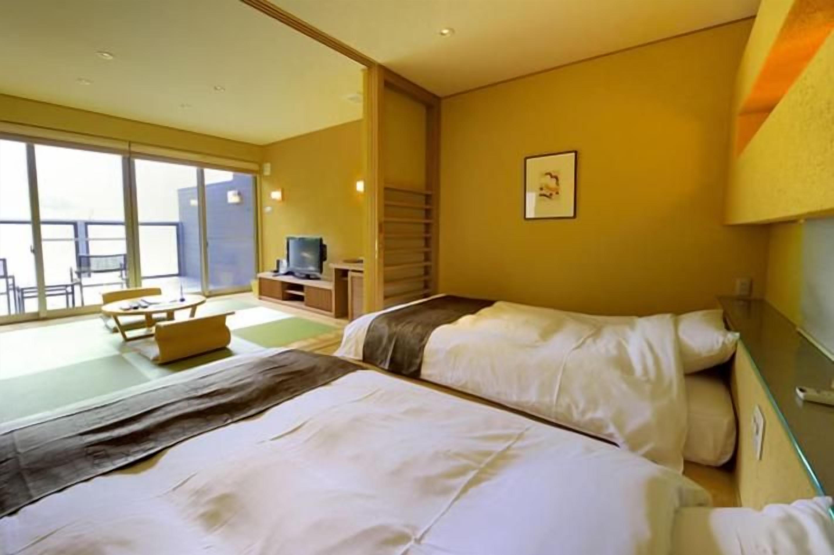 A hotel room with two beds, a television, a desk, and a balcony with seating.