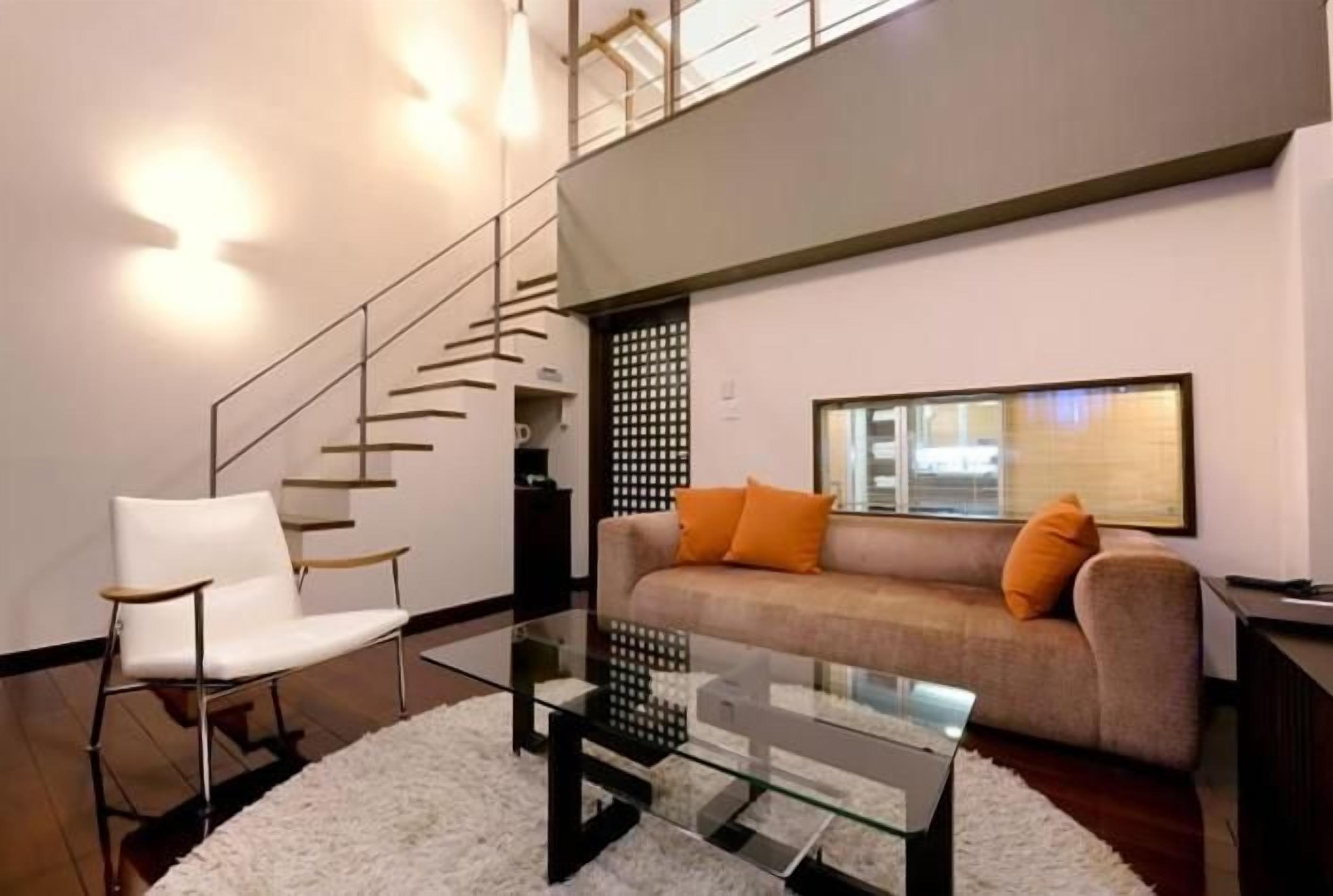 Een moderne woonkamer met een bank, een fauteuil, een glazen salontafel en een trap.