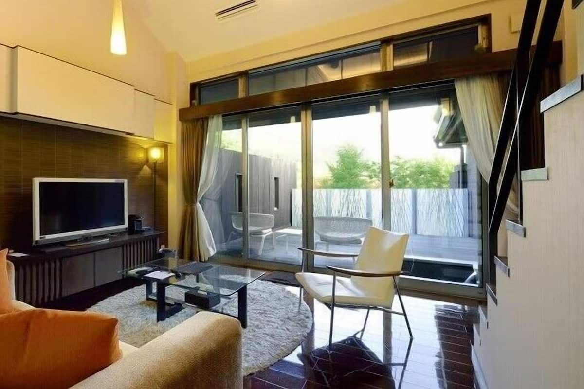 Un salon moderne doté d’un téléviseur à écran plat, d’un canapé, d’une table basse et d’une porte vitrée donnant sur une terrasse extérieure.