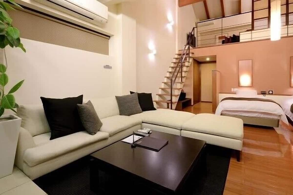 Une chambre d’hôtel moderne avec un canapé, une petite table, un lit, un escalier et une plante.