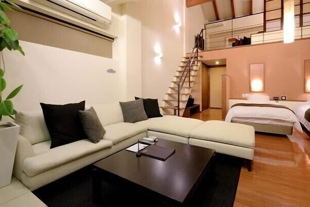 Une chambre d’hôtel moderne avec un canapé, une petite table, un lit, un escalier et une plante.