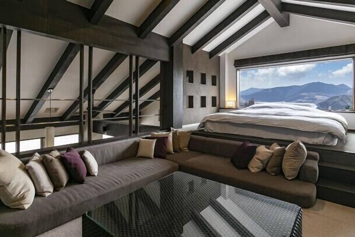 A modern interior with a sofa, a bed, and a large window with a mountain view.