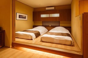 A compact room with two beds, wooden paneling, a framed picture on the wall, and a small cabinet. - Okuyado Buaisou (Yufu)