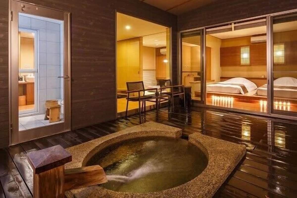 Une chambre dotée d’un jacuzzi, d’un plancher en bois, d’un lit avec une literie blanche et donnant sur un paysage visible à travers une porte vitrée.