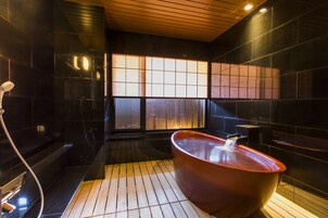 Un baño moderno con suelo de madera, una bañera roja grande y un box de ducha de cristal.