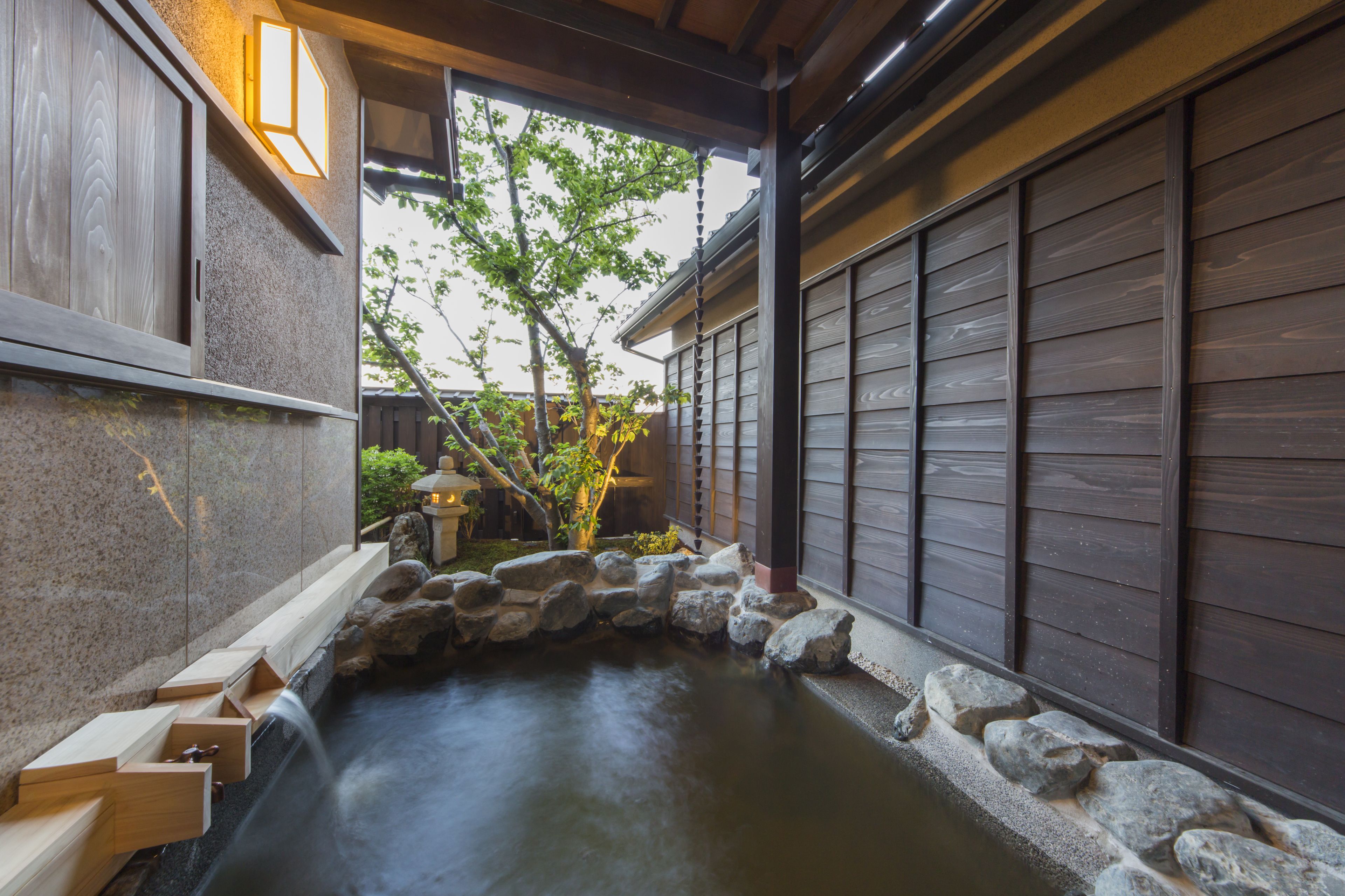 A traditional Japanese garden with a stone water feature, wooden benches, and a view of a residential area.