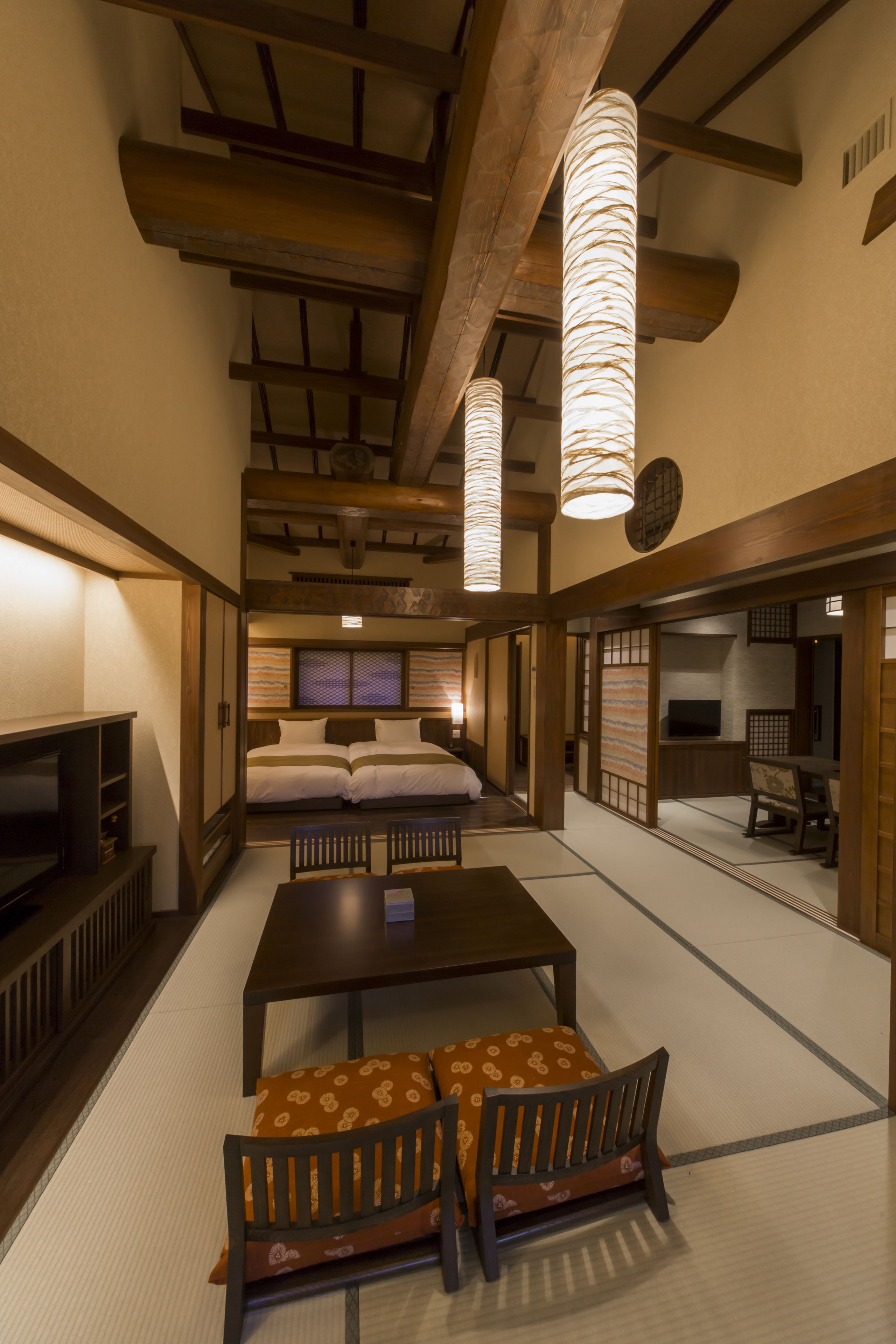 A traditional Japanese room with tatami flooring, a low table with cushions, a television, and sliding doors.