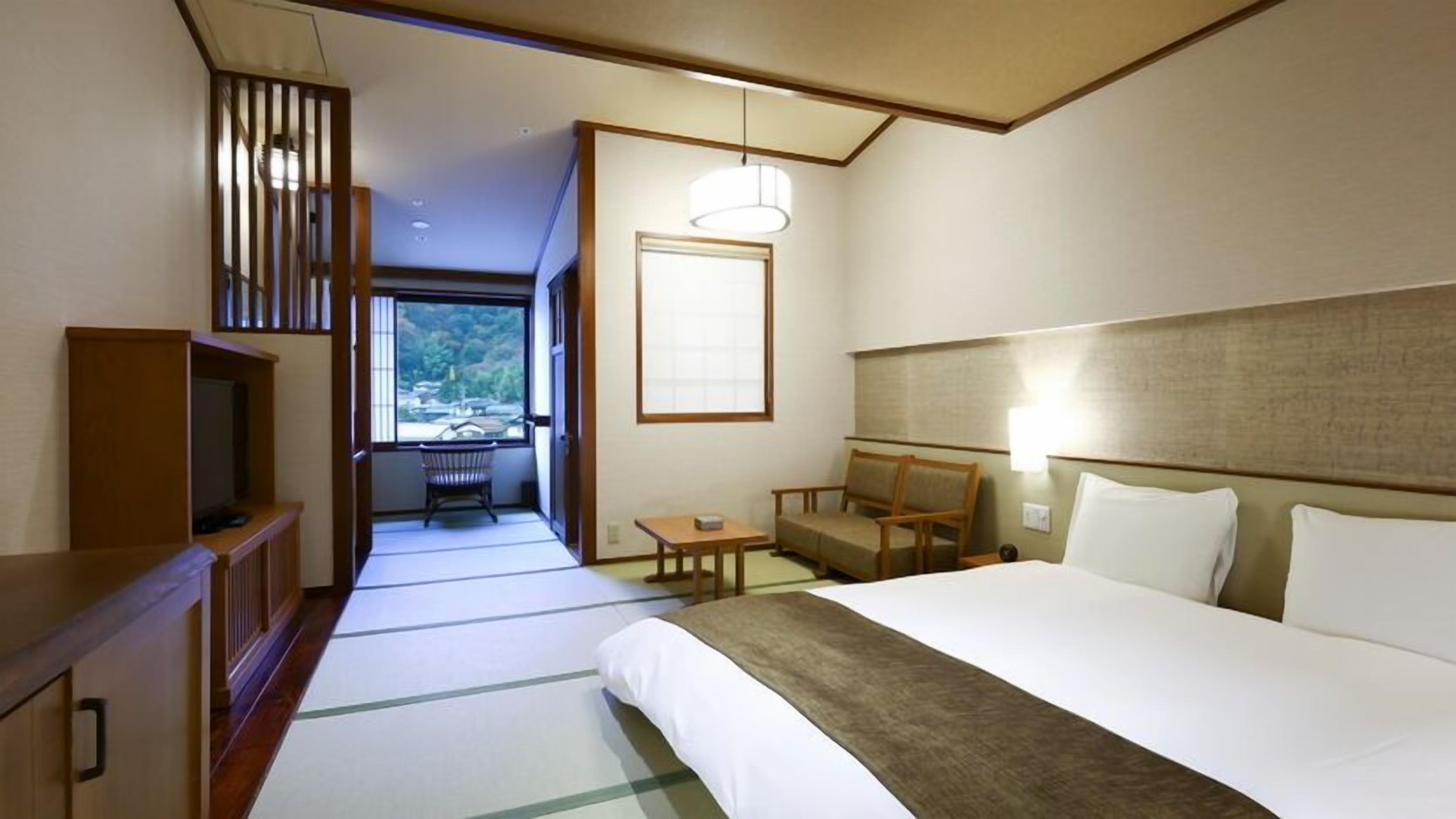 A hotel room with a bed, a desk, a chair, a television, and a view of a balcony.